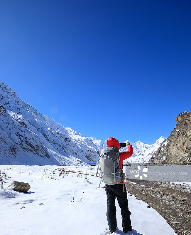 一个背包客在冬天用智能手机拍雪山照片图片素材