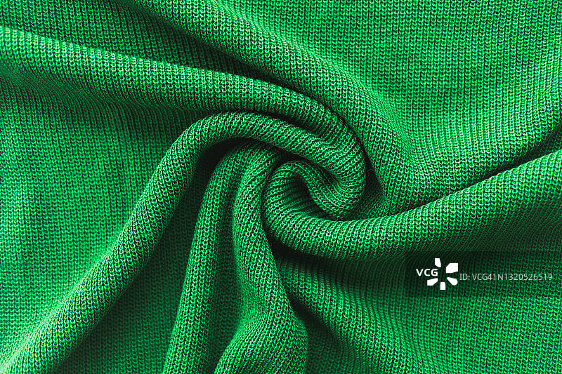 绿色针织毛衣呈旋涡状折叠。平放风格，特写。图片素材