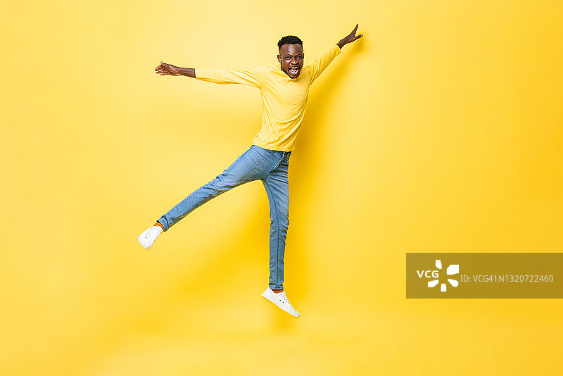 年轻快乐精力充沛的非洲人在孤立的黄色演播室背景上张开双臂和双腿跳跃图片素材