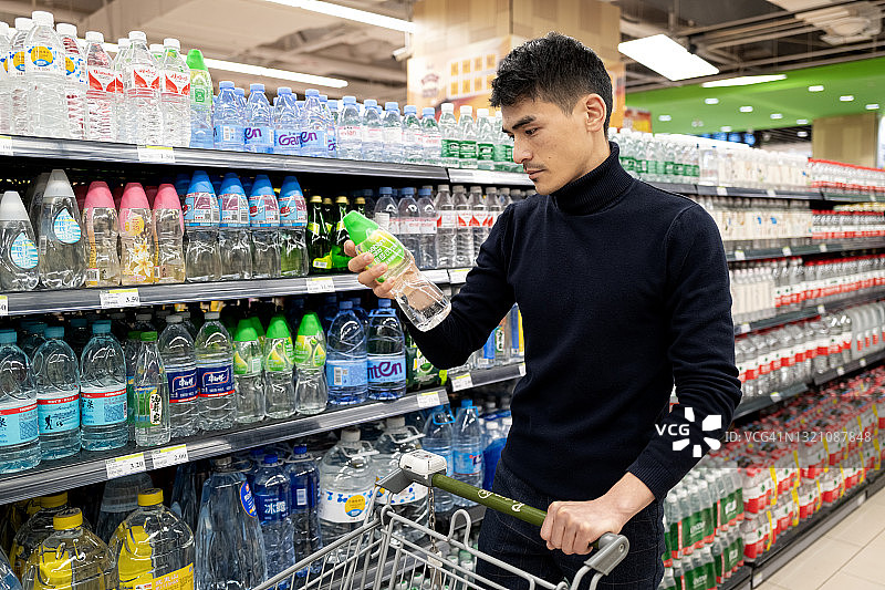 一位男性顾客在杂货店的饮料架前挑选商品图片素材