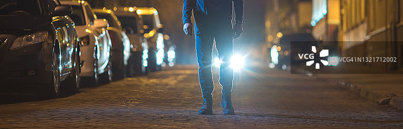 这名男子站在户外的前灯背景上。晚上晚上时间图片素材
