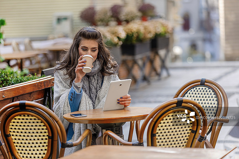 一个年轻迷人的女人正在使用她的数字平板电脑，坐在现代餐厅和她的朋友交流。图片素材