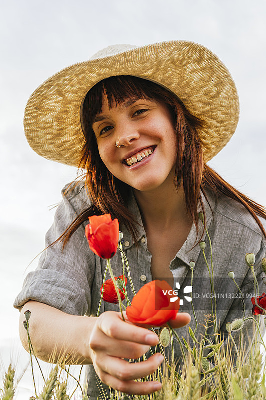 微笑美丽的女人戴着帽子摘罂粟花图片素材