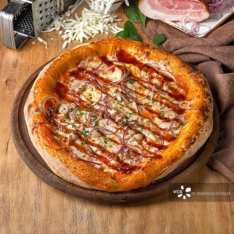 美味的披萨与鸡柳，火腿，培根，香肠，番茄酱和马苏里拉在木制背景。图片素材