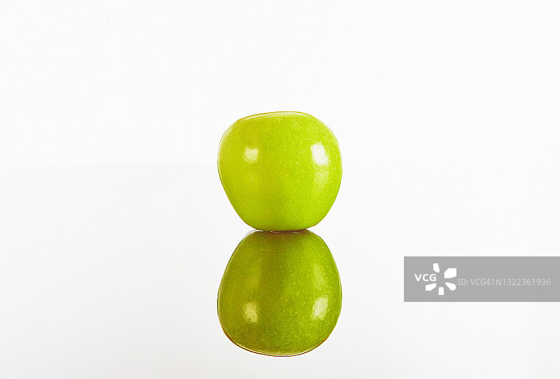 单一的绿色绿苹果，以及它的反射，以朴素的白色背景与复制空间图片素材
