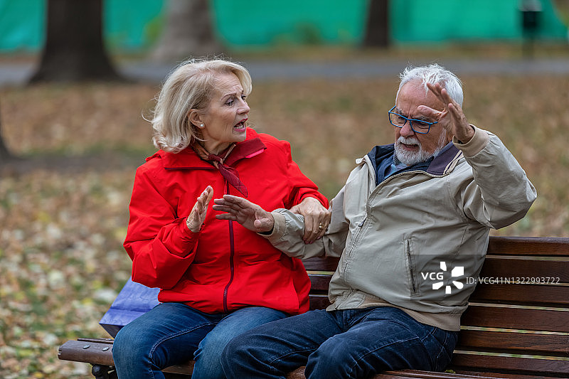 一对不高兴的老年人坐在城市公园里讨论他们遇到的问题。图片素材