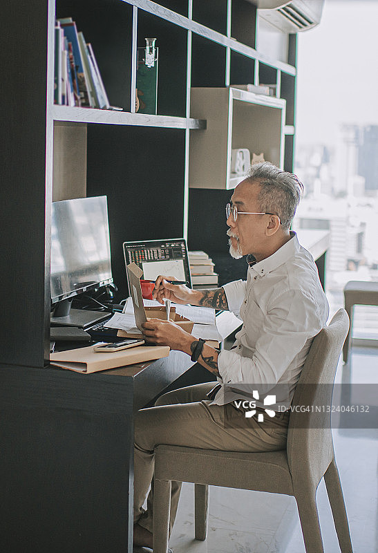 亚洲年长的中国男人，头发花白，一边在家吃外卖，一边用多台电脑监控股市走势图片素材