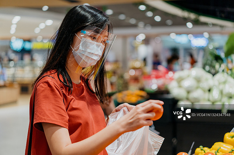 亚洲妇女戴着面罩和面罩在超市购买新鲜的西红柿图片素材