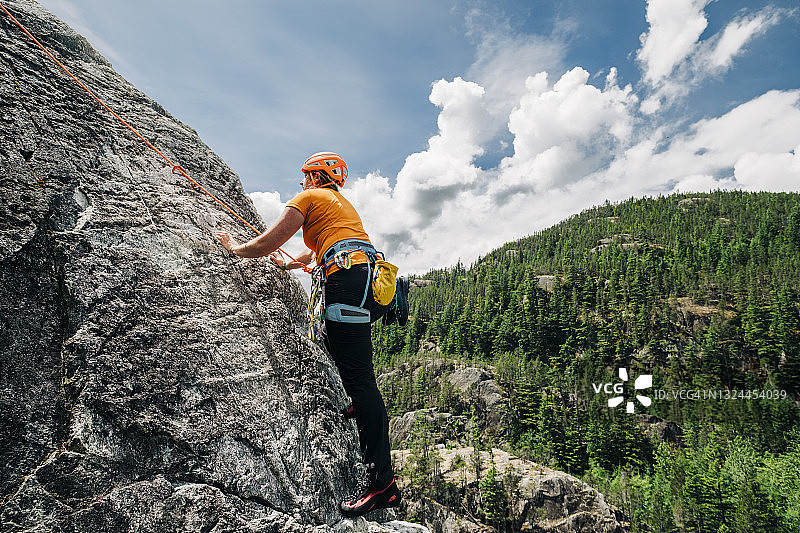 女攀岩者戴着攀岩头盔和挽具爬向岩壁一侧的岩架图片素材