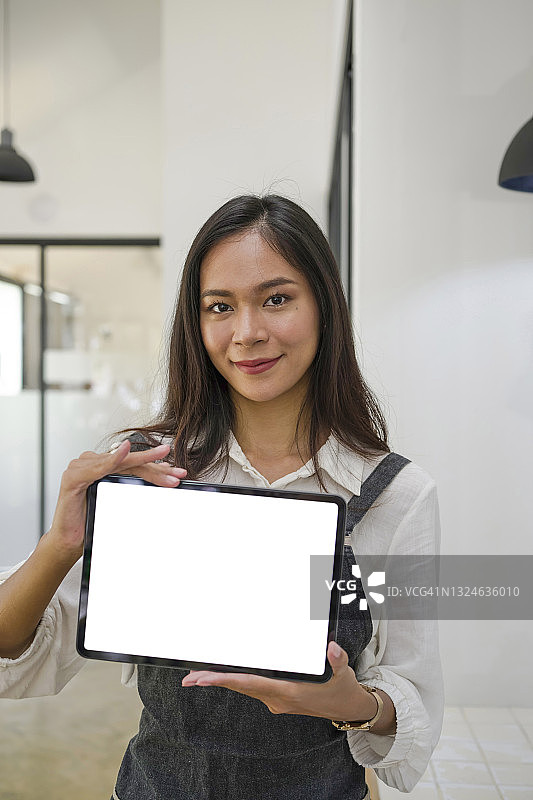 年轻愉快的女老板站在咖啡店里展示数码平板电脑。图片素材