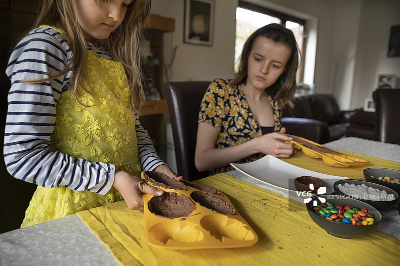 儿童和青少年在餐桌上从硅胶模具中取出巧克力复活节彩蛋图片素材