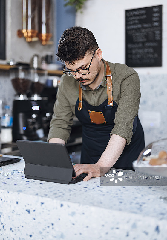 专业的咖啡师站在咖啡店的柜台和使用数字平板电脑的肖像图片素材
