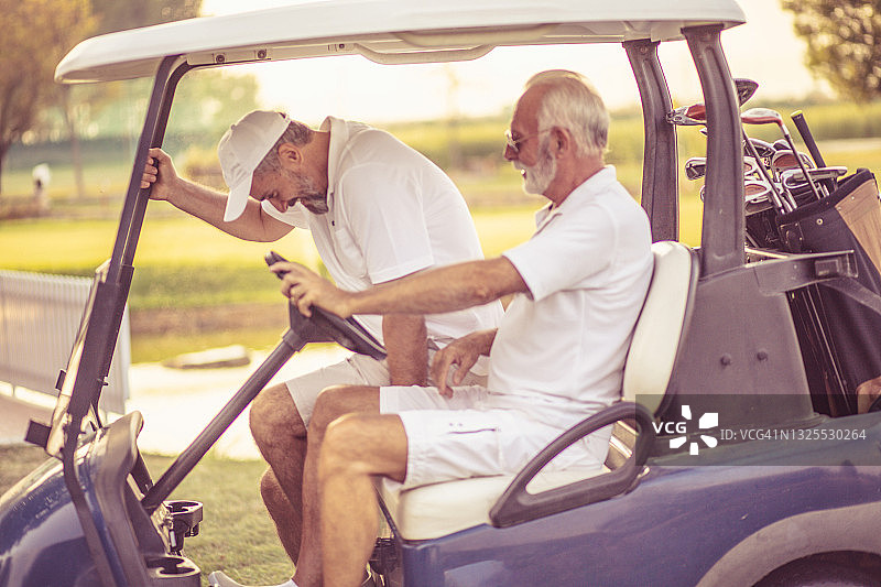 两个快乐的老朋友坐在高尔夫球车里。图片素材