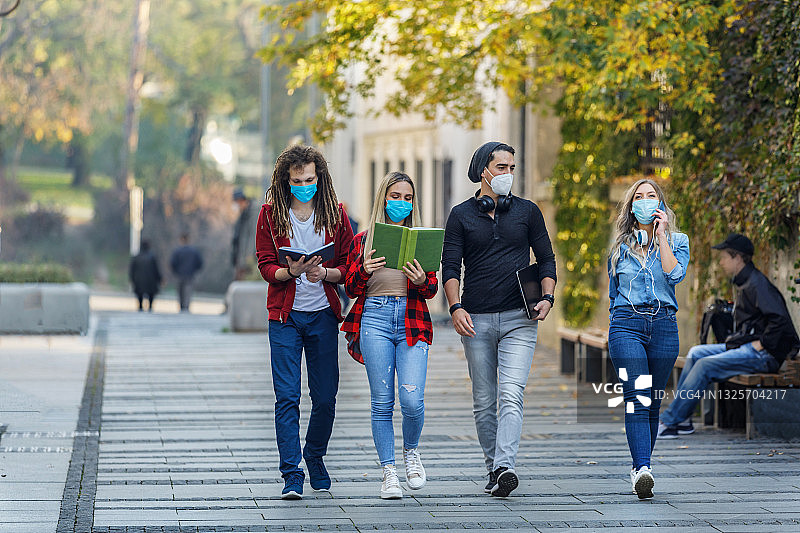 一群戴着防护口罩的学生走在新冠肺炎疫情的城市里。图片素材
