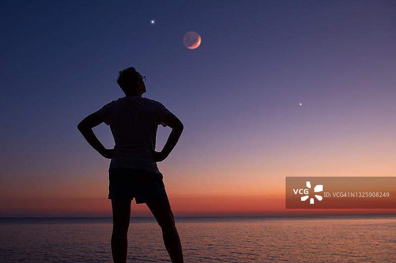 一个人的剪影看着月亮和星星在海上地平线。图片素材