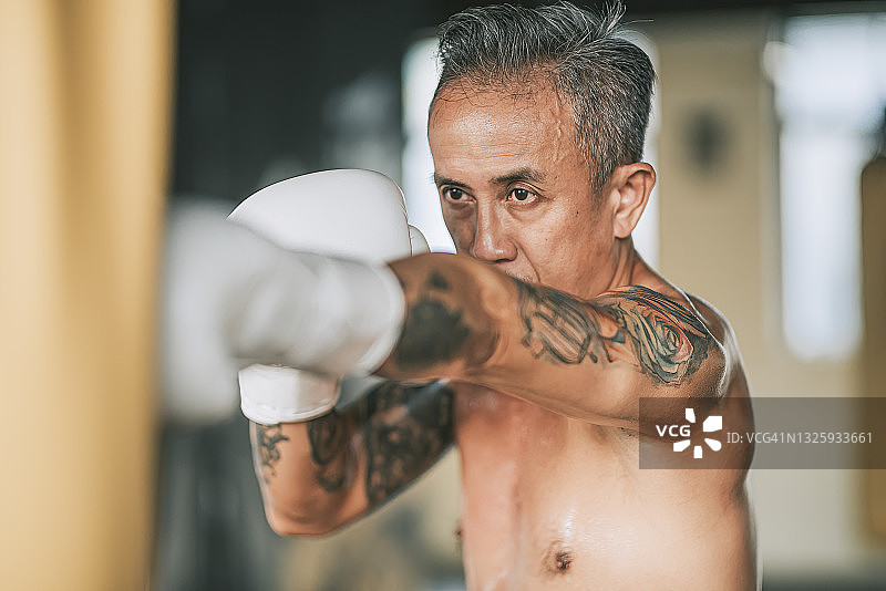 极限运动亚洲资深男子泰拳拳手在健身俱乐部沙袋练习图片素材