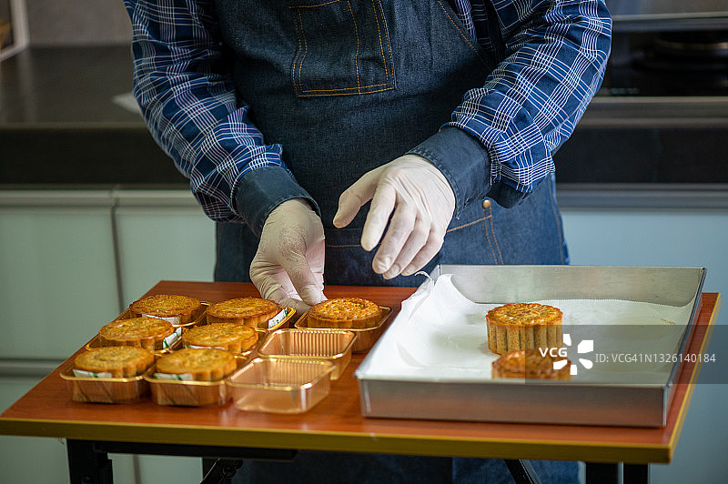 一位亚洲男性面包师把自制的中国月饼放在金色的塑料容器上图片素材