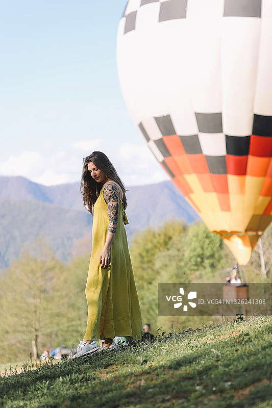 一个快乐孤独的年轻女游客，穿着明亮的黄色衣服，在绿色的茶园森林中散步和远足，背景是山里的热气球图片素材
