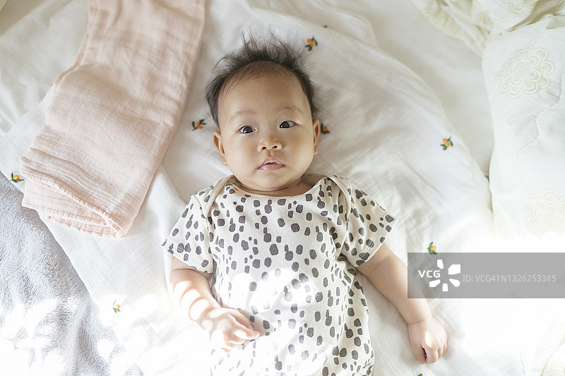 俯视图面部表情亚洲女性婴儿(4-5个月)在舒适的床上为婴儿图片素材