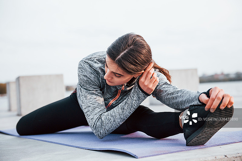 年轻的运动女孩在户外健身垫上做瑜伽练习白天在湖边图片素材