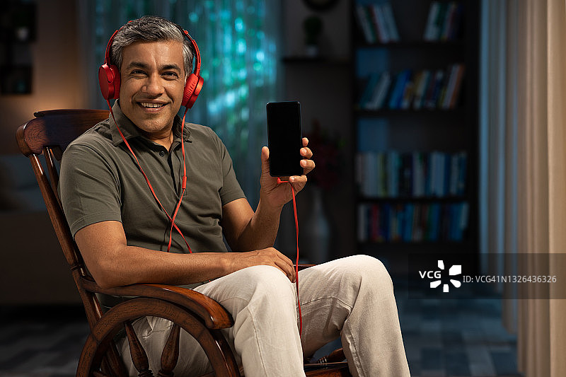 一个成熟的男人坐在摇椅上听音乐，家里的手机显示空白:-库存照片图片素材