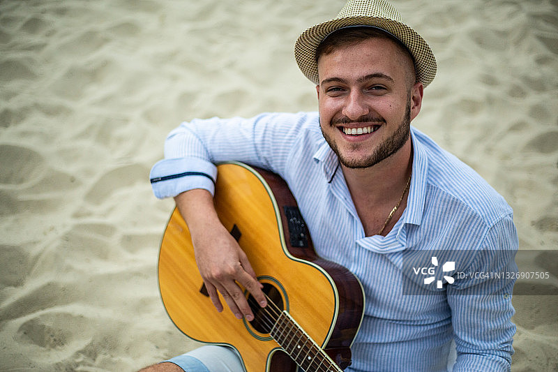 一个年轻英俊的男人在海滩上弹吉他。图片素材