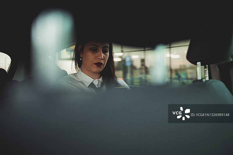 一位年轻的黑发商务女性坐在汽车后座上，去参加一个商务会议并使用手机。图片素材