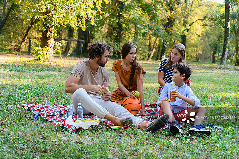 年轻的父母和他们可爱的儿子和女儿在野餐。图片素材