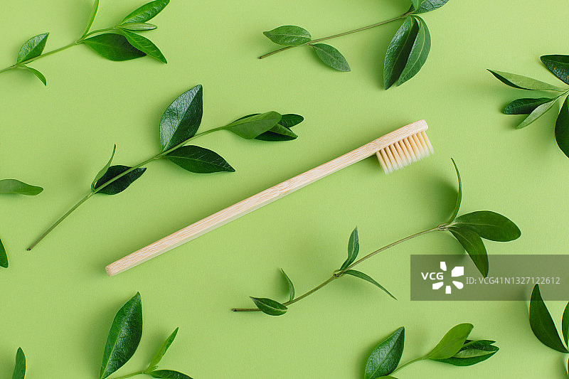环保的竹制牙刷，绿色的枝叶，绿色的背景。“零浪费”。天然有机浴室美容产品概念。平躺，俯视图。图片素材