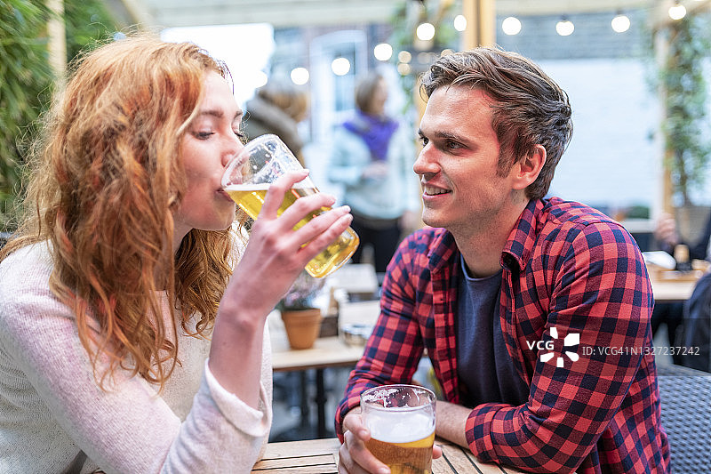 一个男人看着在酒吧里喝啤酒的女朋友图片素材