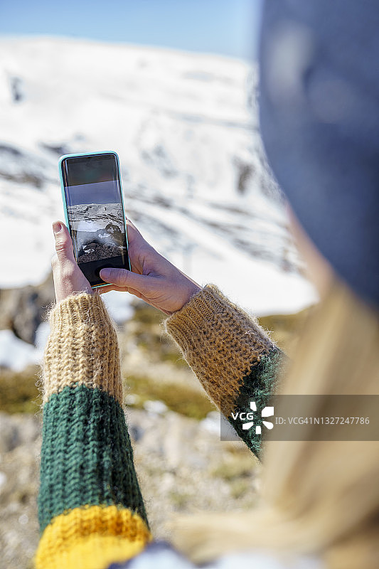 一名女子在冬天用手机拍摄雪山图片素材