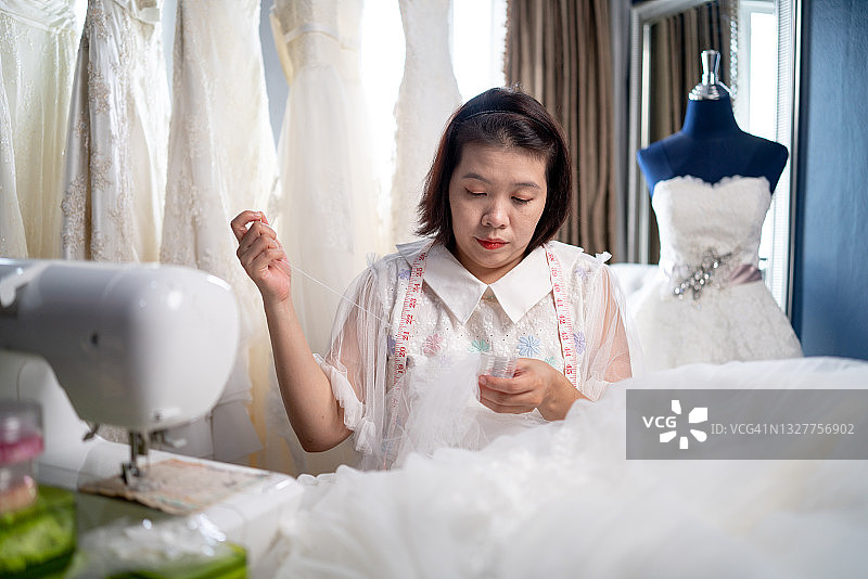 裁缝店的老板在婚纱房，在店里缝一件白色的婚纱。图片素材
