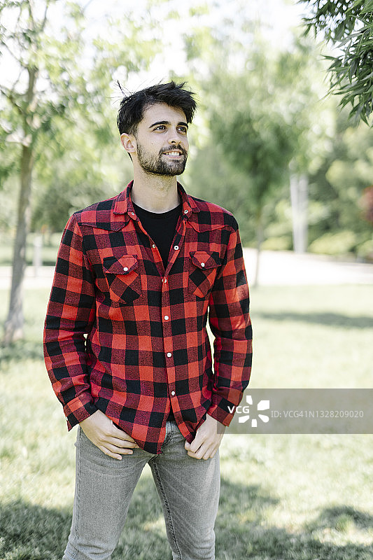一个年轻男子的肖像穿着格子衬衫在一个公园看向别处图片素材