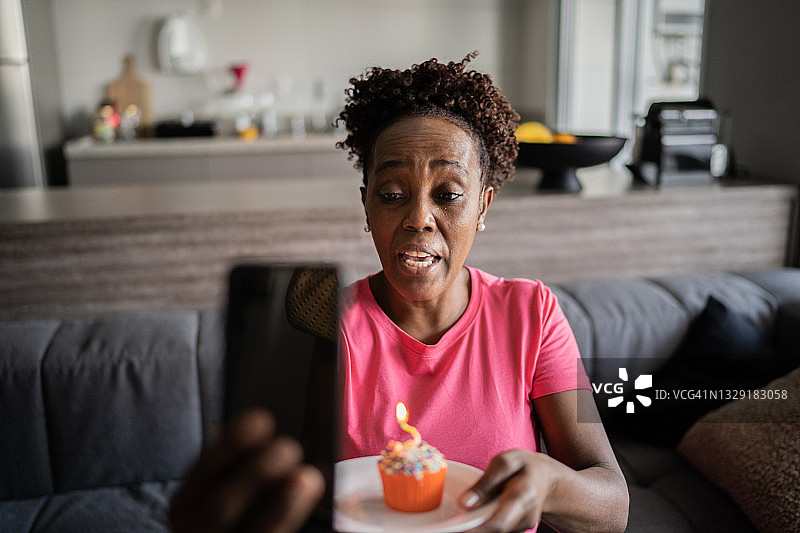 成熟的女人在家里用智能手机打视频电话庆祝生日图片素材