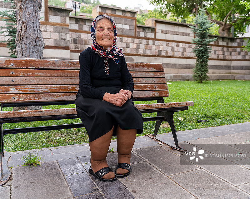 老妇人坐在长凳上，微笑着看着镜头图片素材