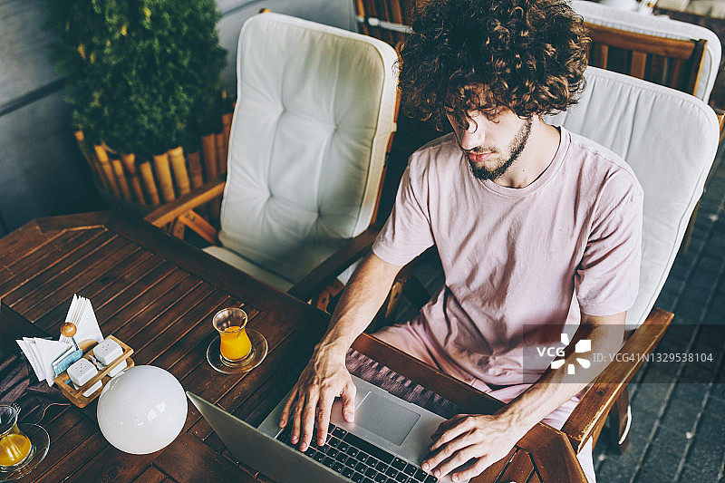 一名19岁的年轻人正坐在咖啡馆里，手里拿着一台笔记本电脑，他的注意力正集中在屏幕上。图片素材