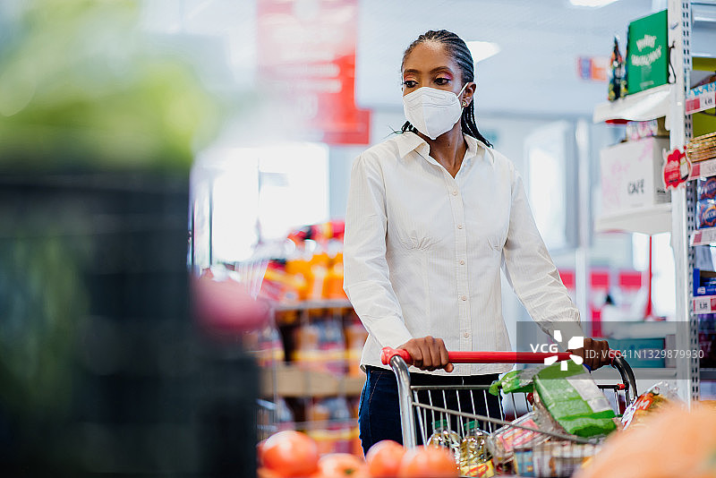 一名妇女戴着冠状病毒口罩在超市购物。图片素材