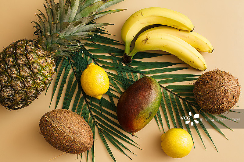 夏季热带的概念。绿色的棕榈叶和菠萝，香蕉，椰子，芒果，柠檬在米色的背景上。平铺，俯视图图片素材