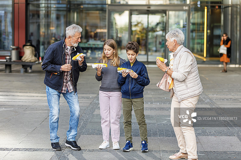 男孩和女孩和祖父母在城市里散步，吃着玉米。图片素材