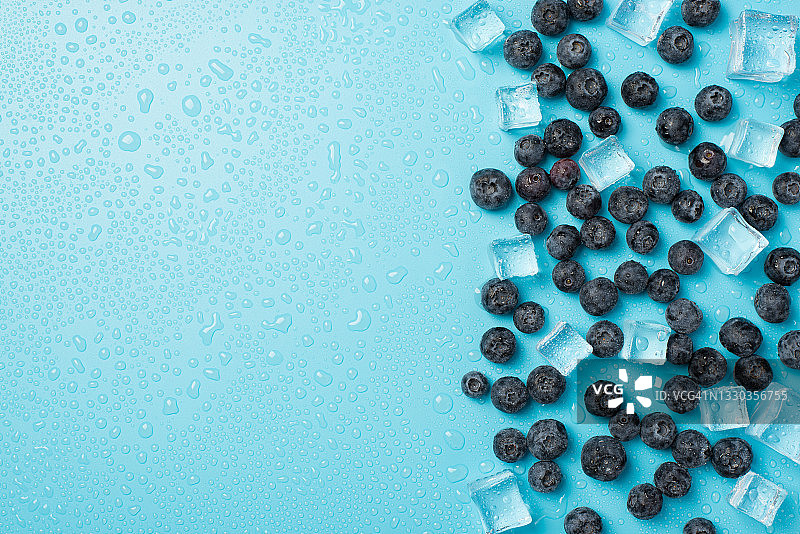 上面的照片是一堆蓝莓，冰块和水滴孤立的蓝色背景与空白图片素材