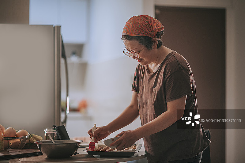 亚洲华人中年妇女戴着头巾在厨房的花生饼干上刷蛋黄图片素材