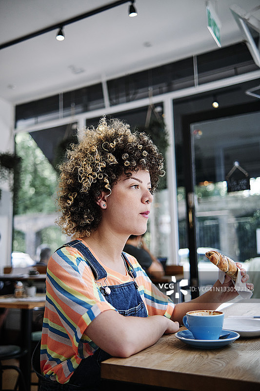 一个女人坐在咖啡馆的桌子边吃羊角面包图片素材