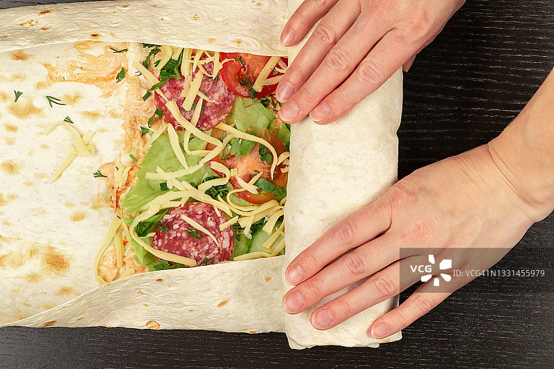 女人们用手把新鲜的蔬菜沙拉和奶酪包在皮塔面包里。在木桌上做沙瓦玛图片素材