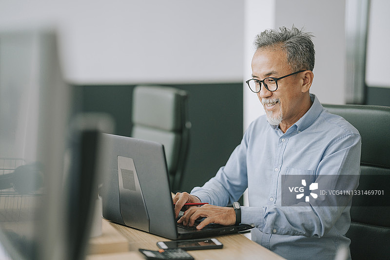 有胡子的亚洲华人高级男子在办公室用笔记本电脑打字图片素材