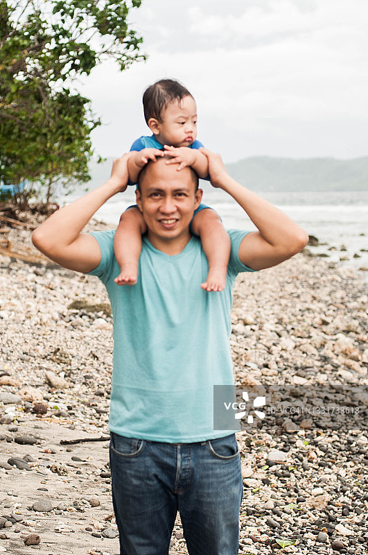 在沙滩上，一位年轻的东南亚父亲把儿子扛在肩上图片素材