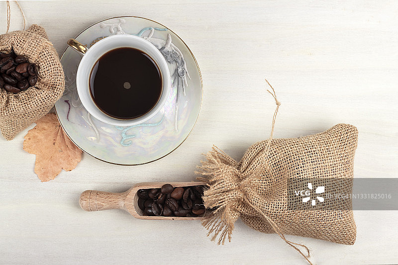咖啡杯，麻袋烘焙咖啡豆，浅白色乡村背景上的秋叶。图片素材