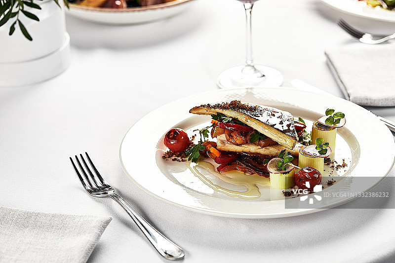 烤鲈鱼和炸西红柿，特写的烤鱼在一个轻的盘子，烤鲈鱼和一杯葡萄酒，假日的餐桌图片素材