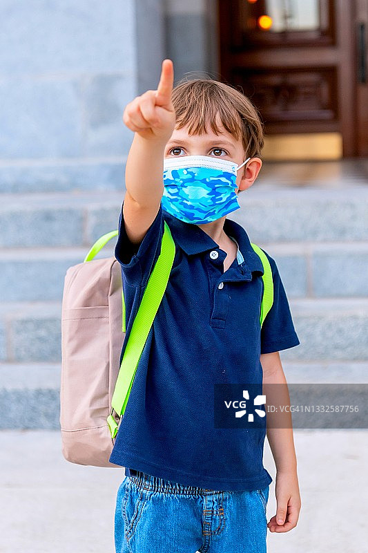小男孩背着书包回到学校，在学校门口摆姿势图片素材