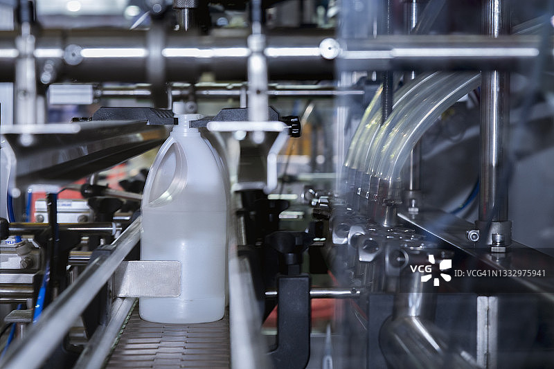 在工厂灌装机的传送带生产线上的白色塑料加仑或瓶。工业和技术概念。图片素材