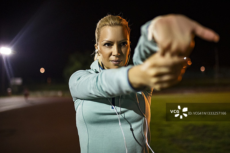 运动女子夜间在跑道上伸展手臂图片素材